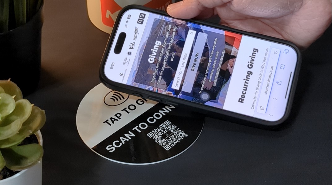 A phone tapping the Tap to Give plaque opens the church giving page