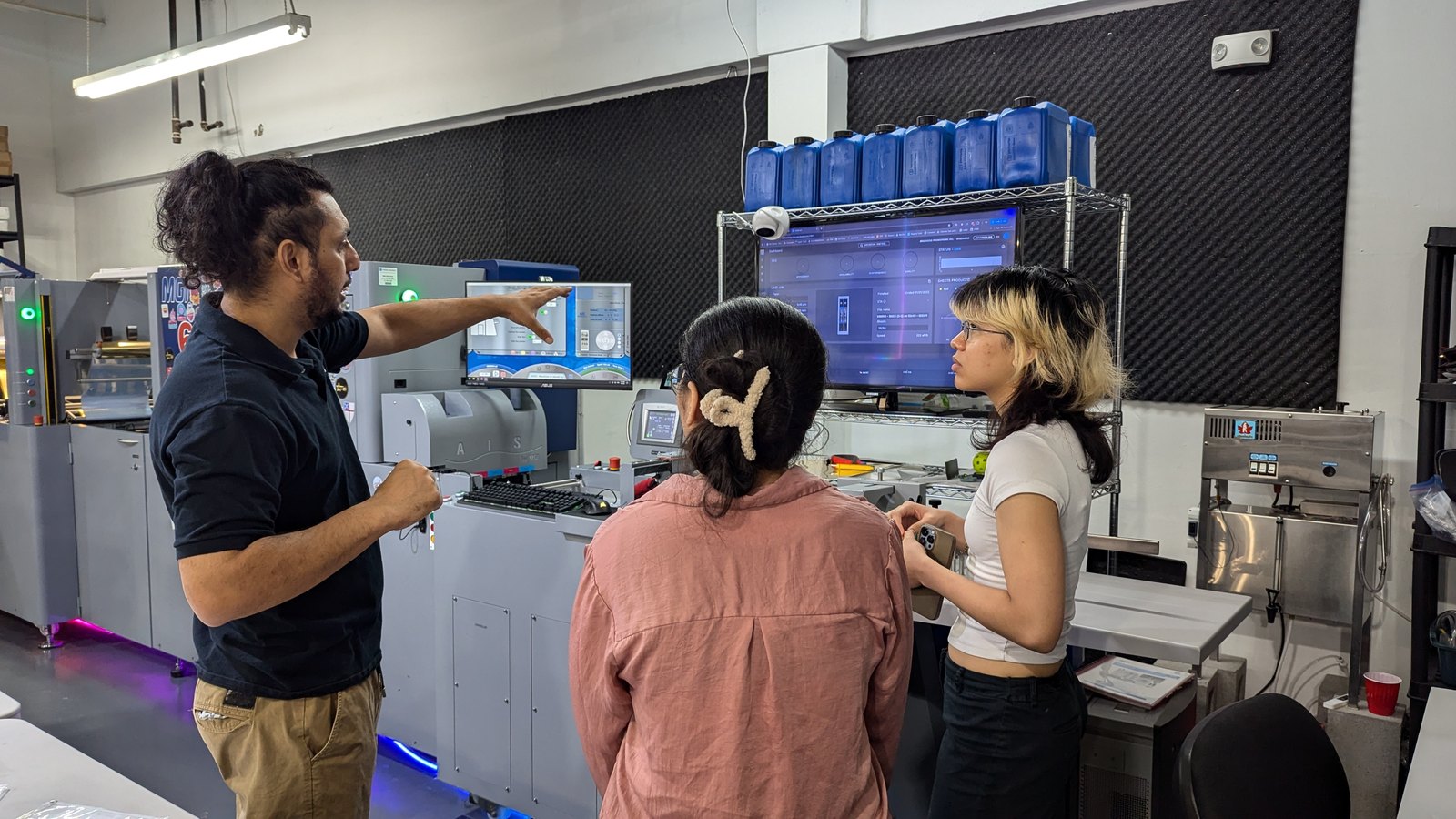 Karan explaining a press screen to two interns beside the digital press