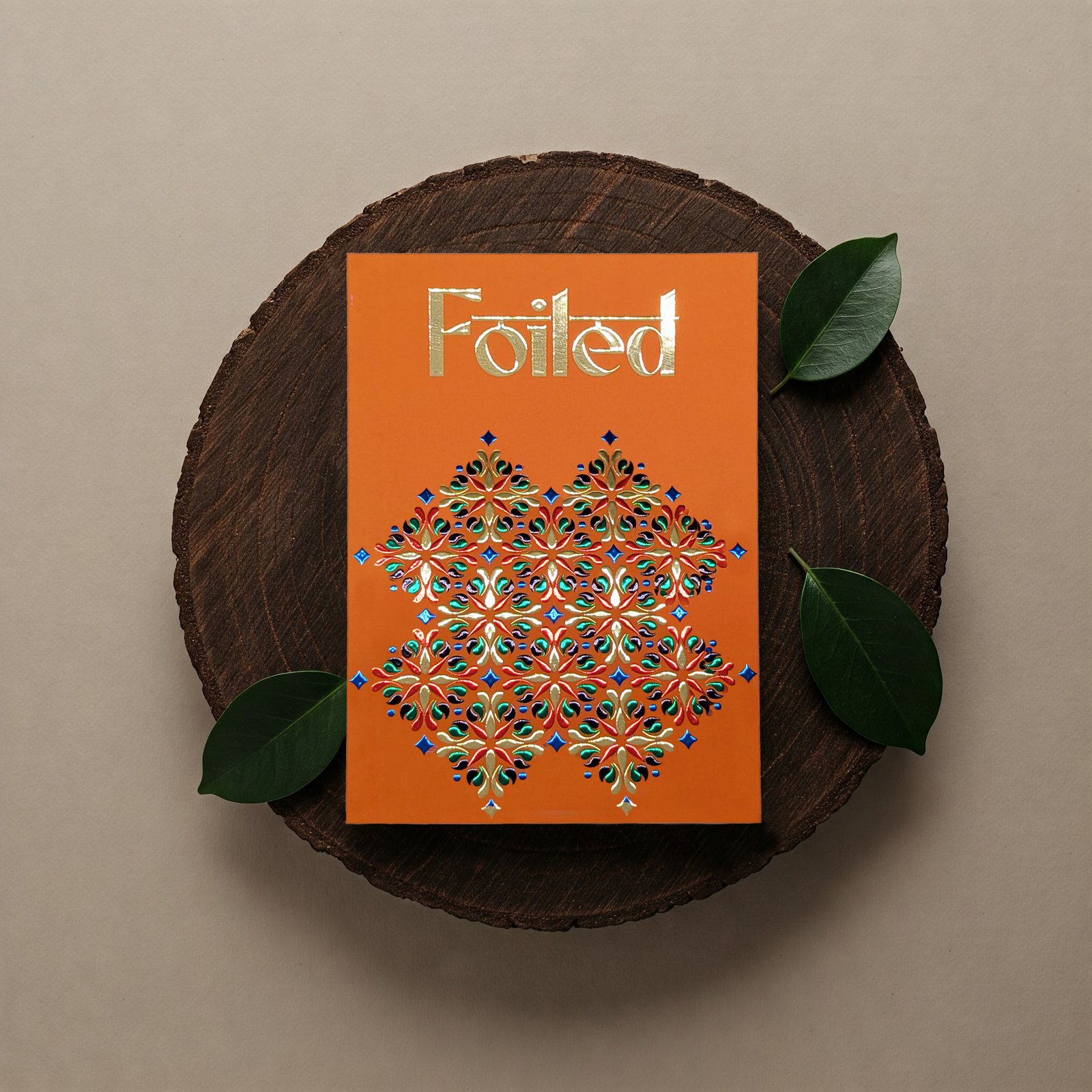 Orange card titled Foiled, with a multicolour raised foil pattern, on a wooden board with leaves